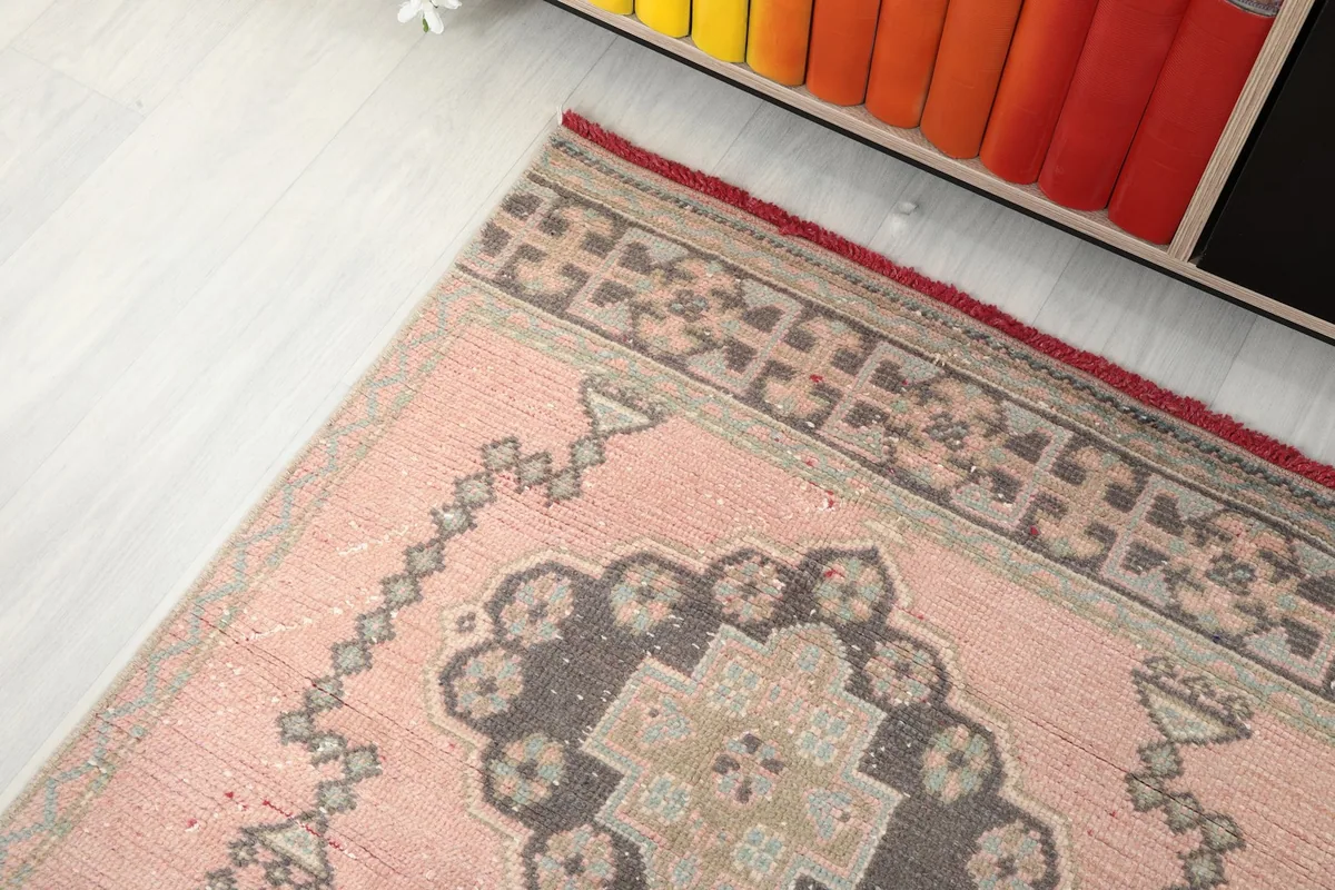 Angle view of the rug's end section, showing the border design and a gray medallion near a bookshelf.
