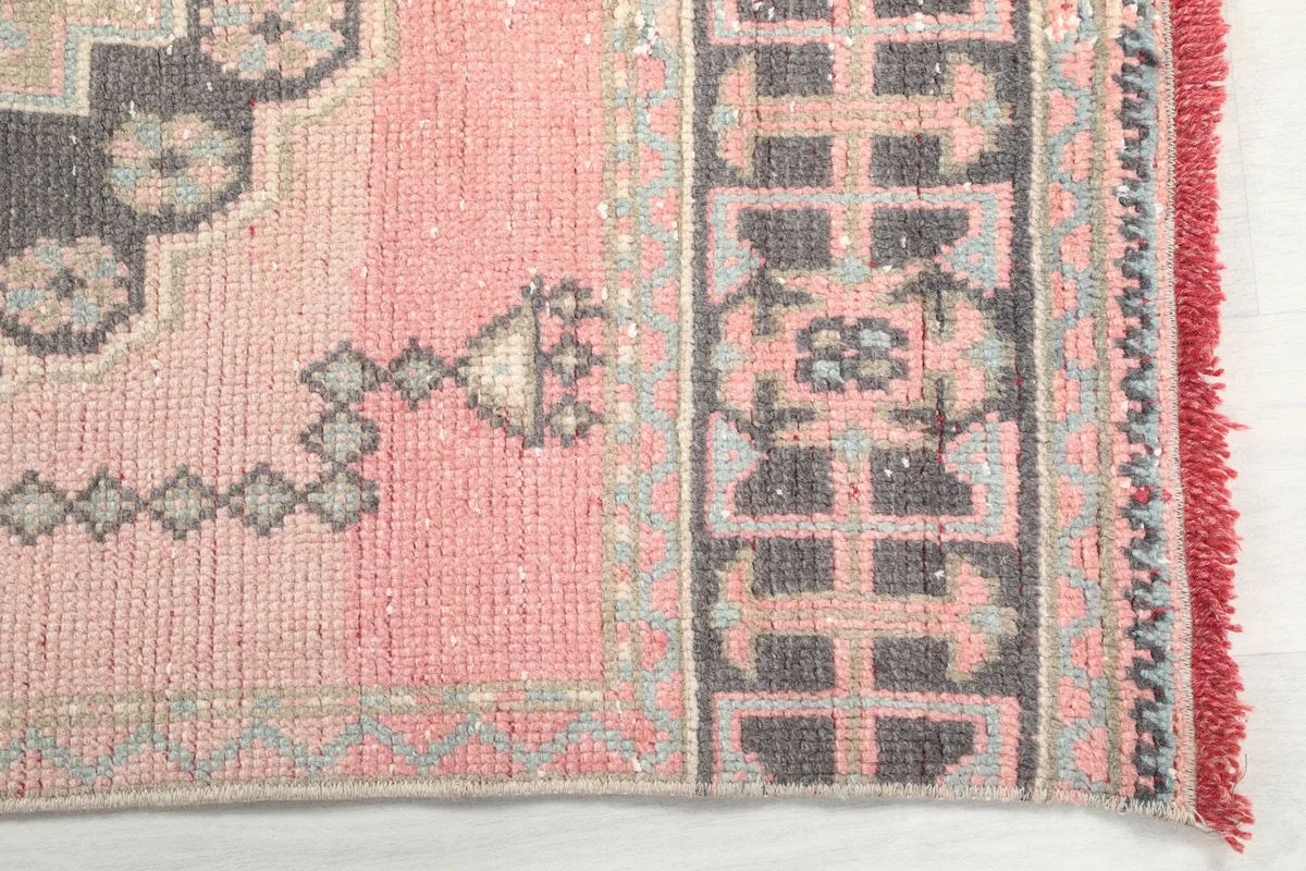 Detailed view of the rose rug's border and a corner, showing the hand-knotted construction and fringe.