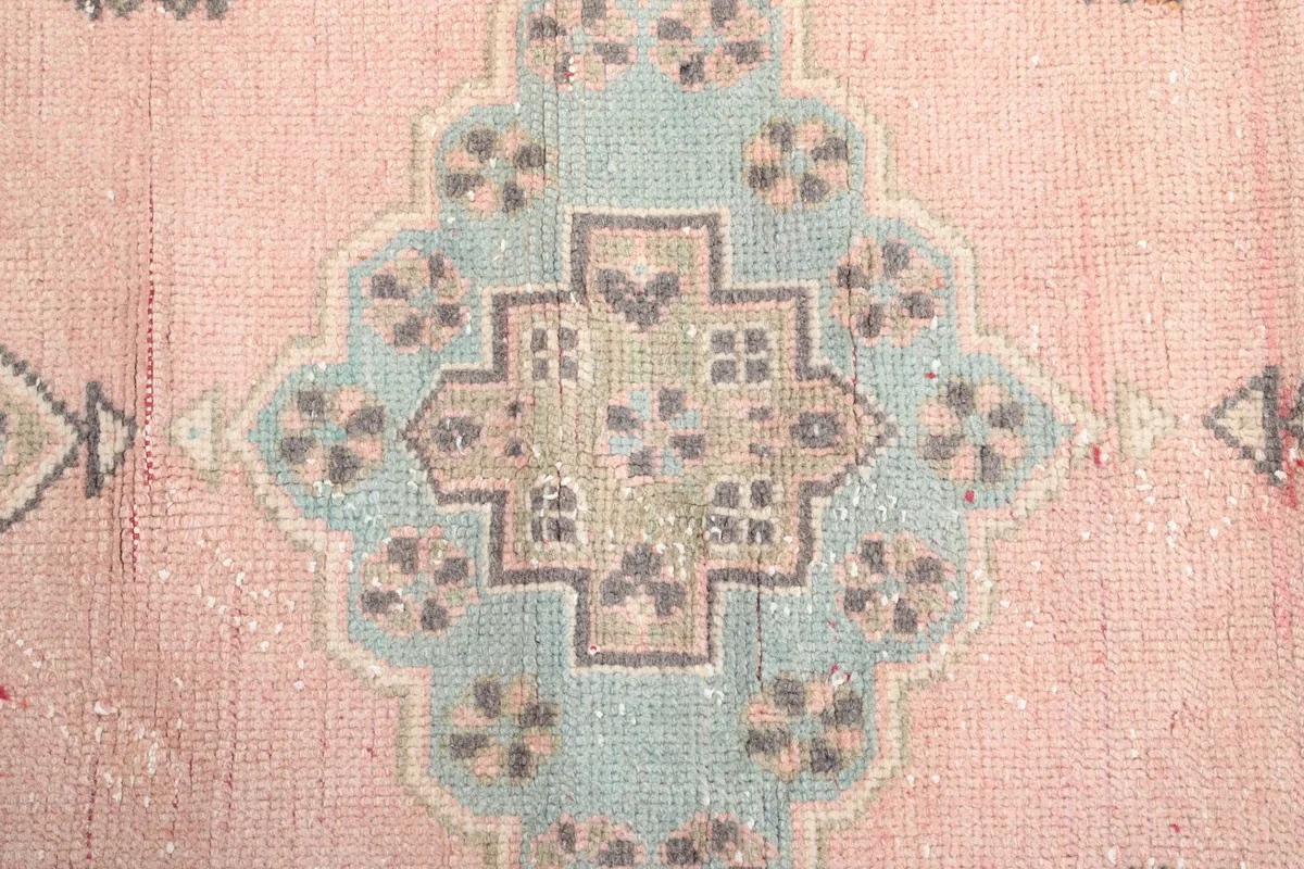 Close-up of a blue and beige geometric medallion on the rose field of the runner rug.