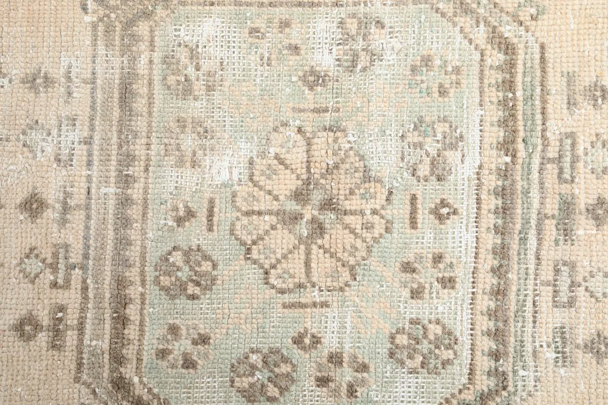 Close-up of a central geometric medallion with olive and tan tones, showing knot detail and patina.