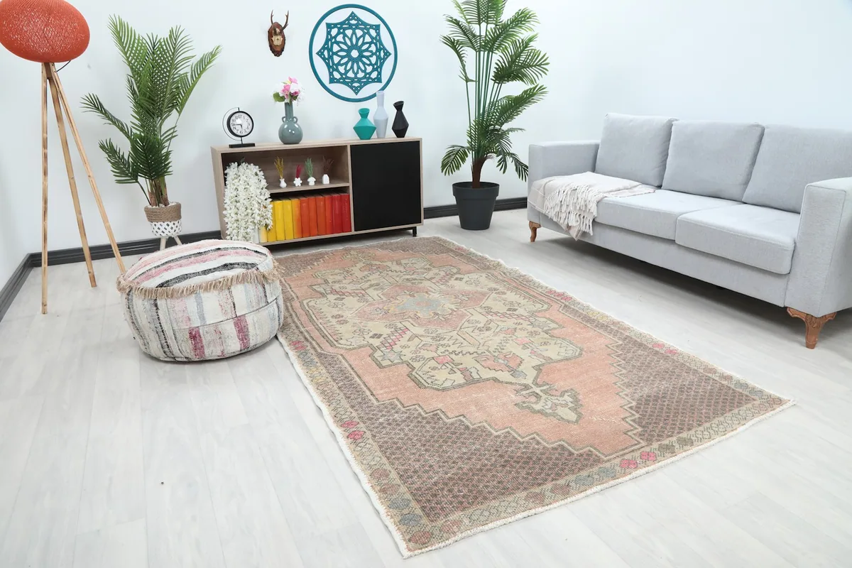 Angle view of the rose and brown vintage rug in a living space, showing its size in relation to a sofa and ottoman.