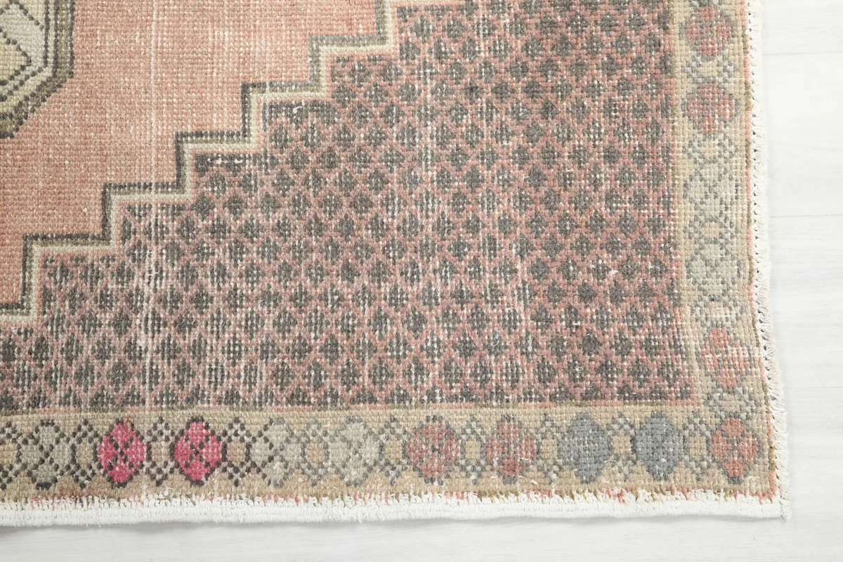 Detailed view of the rug's brown border and a corner of the rose field, highlighting the geometric motifs and fringe.