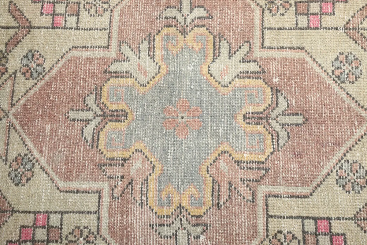 Close-up of the central medallion, displaying the faded rose, beige, and gray colors and the hand-knotted texture.