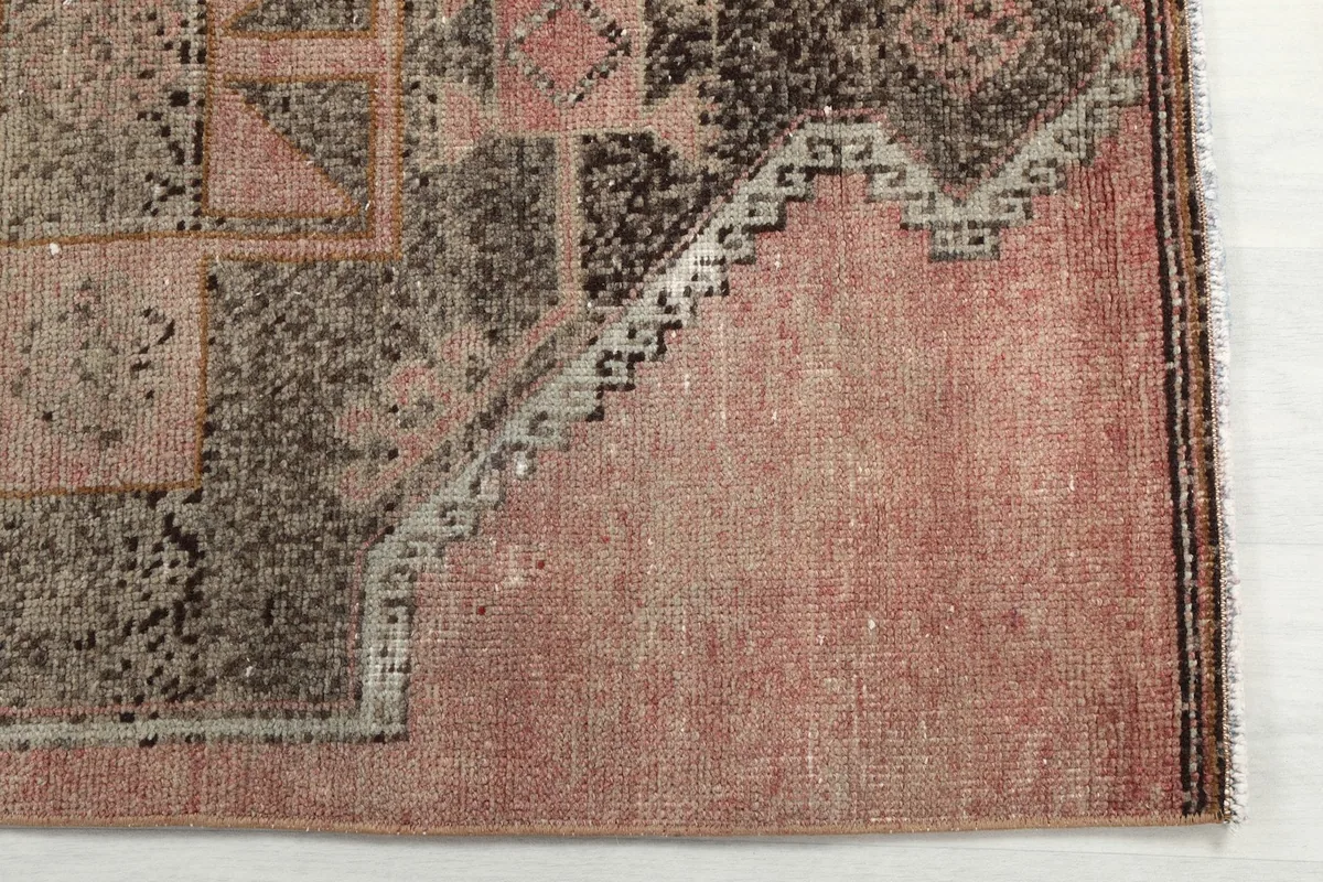 Detailed view of the rug's corner, showing the gray and charcoal geometric design on a rose background