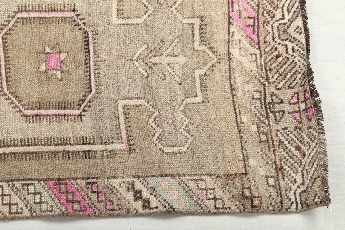 Detailed shot of the rug's border and a corner motif, revealing the pink and beige patterns.