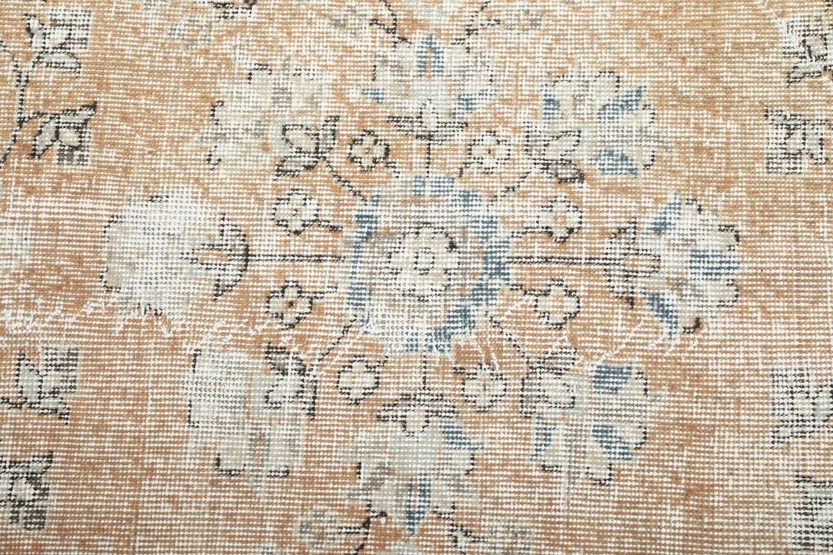 Detailed view of a central floral motif in blue and gray on the beige background, showing pile wear