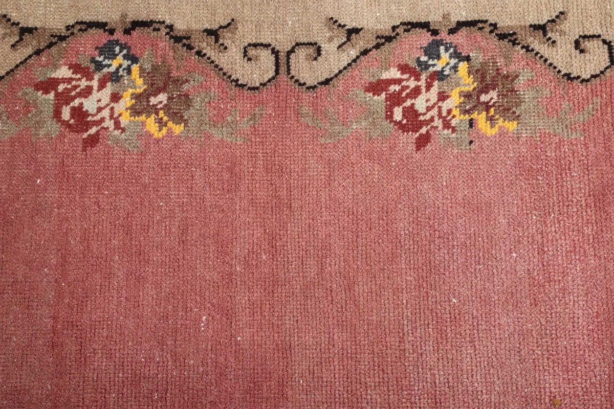 Close-up of the pink rug's field and a section of the beige border with multicolor floral patterns
