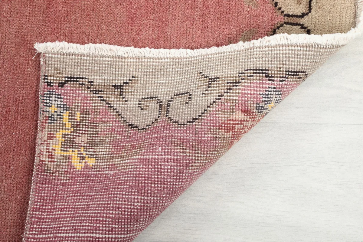 Close-up of the pink runner rug's corner, revealing the wool pile and cotton foundation