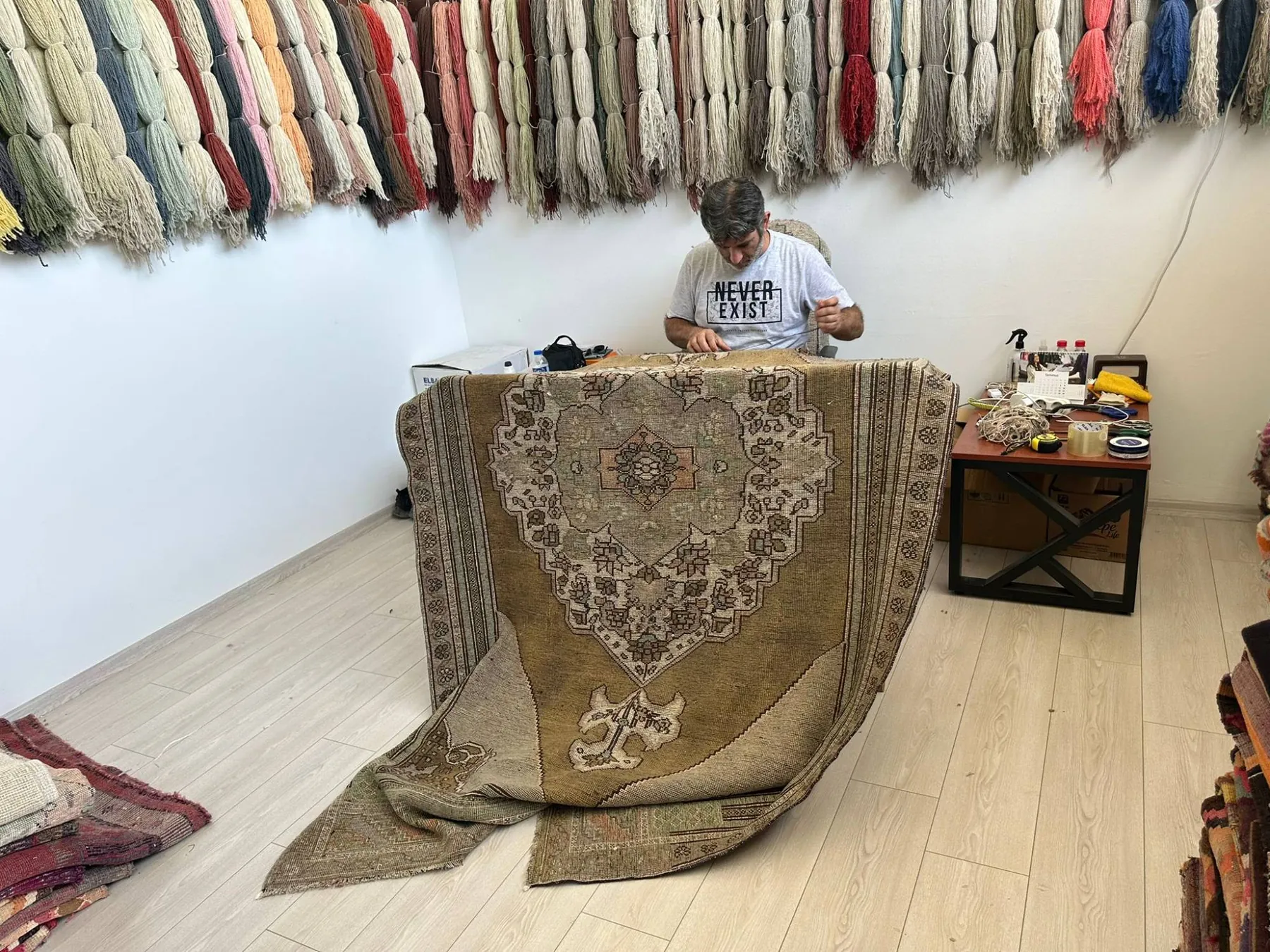 Restoring a vintage rug by hand in front of skeins of natural wool